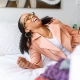 Woman in the pink jacket and wearing glasses laughing on the bed