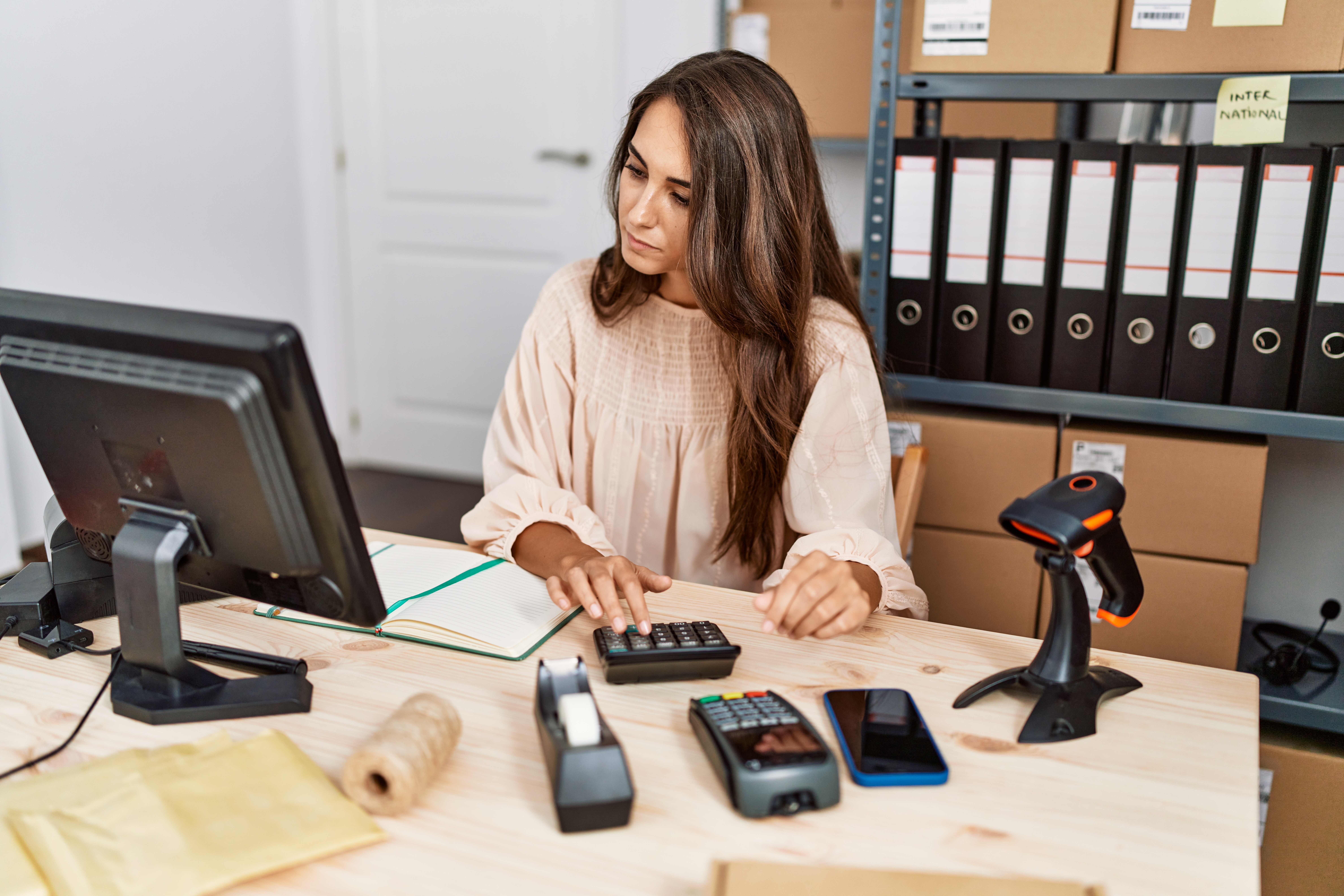A hispanic small business owner sits at an office desk looking at a laptop, working on strengthening operational efficiency before trying to grow her business.