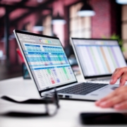 Hands typing on a laptop showing spreadsheets.