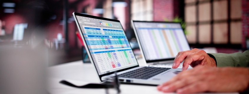 Hands typing on a laptop showing spreadsheets.