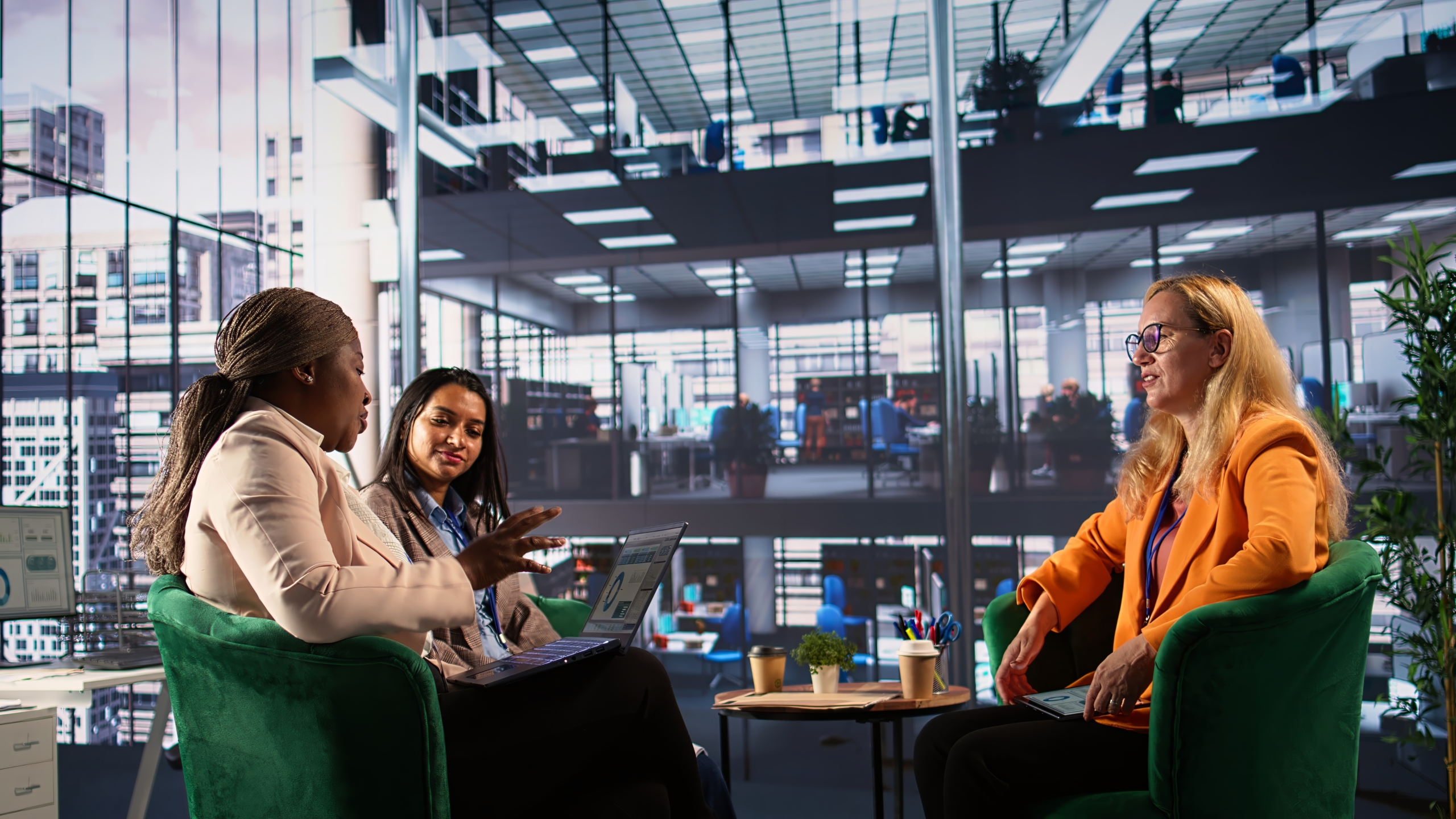 Three women are in discussion around a table in an office building.