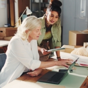 Laptop,,Supply,Chain,And,Meeting,With,Women,In,Office,For Two businesswomen in an office discussing business financing strategies and growth cycles.