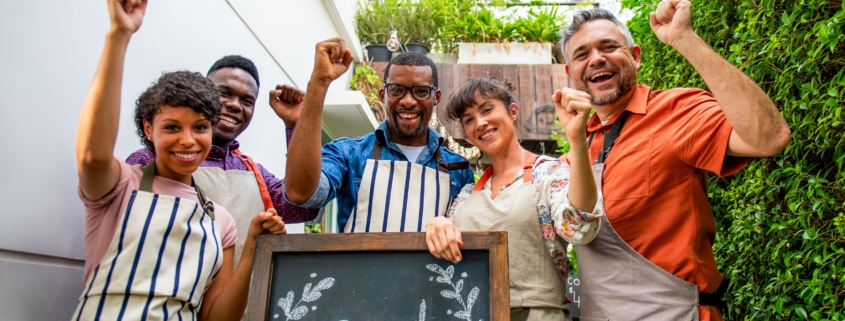 A diverse group of workers with aprons on elaborate the opening of a new business.