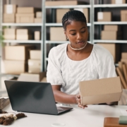 Black,Woman,,Laptop,And,Logistics,With,Box,For,Small,Business Black female entrepreneur evaluating financing options and loan-to-value ratio for small businesses at her desk.