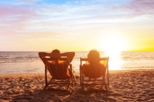 Couple sitting in beach chairs facing the water and sunrise.