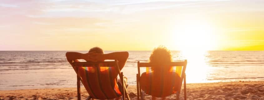Couple sitting in beach chairs facing the water and sunrise.