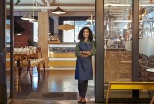 Woman standing in front of her store wearing an apron.