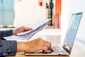 Two hands are near a laptop. One of the hands is pressing paper pulp product.