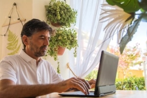 Man with arms casually extended typing in front of several plants