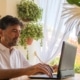 Man with arms casually extended typing in front of several plants